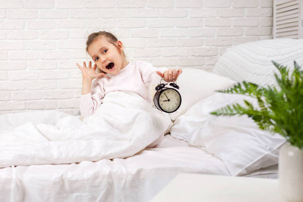 Little girl in pyjamas with clock - Foto, Bild
