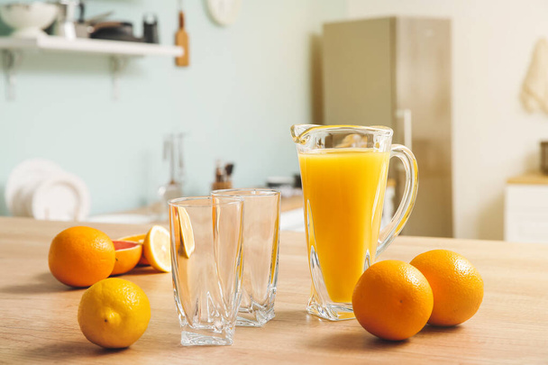 Jug of fresh fruit juice and empty glasses on table - Фото, изображение