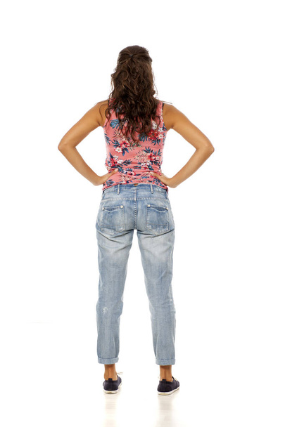 vista posterior de la mujer joven con pantalones vaqueros rotos de pie sobre fondo blanco
 - Foto, Imagen