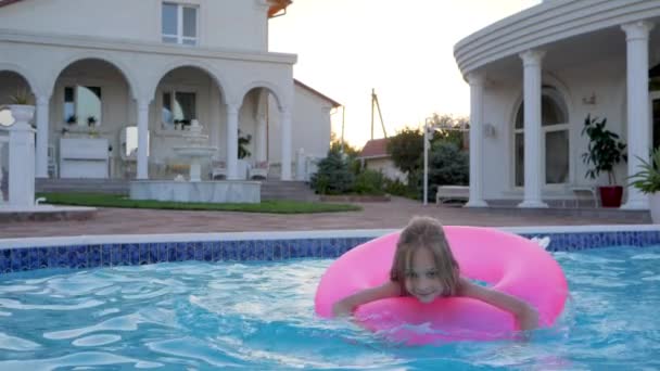 Mooi meisje zwemmen op opblaasbare roze ring in zwembad, Zomervakantie in Mansion, Besproeiing van water, - Video