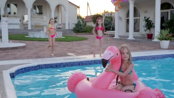 Klein meisje In badpak springen in de zomer zwembad, Mooi kind in opblaasbare flamingo zwemmen in het zwembad, vrolijke sprong - Video
