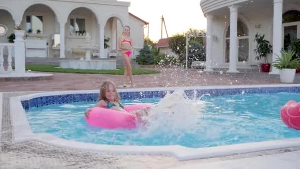 Μικρό κορίτσι που κολυμπούν σε φουσκωτό δαχτυλίδι και δίνει νερό πιτσιλιές στο Poolside, Πλούσιες μικρές αδελφές περνούν το καλοκαίρι - Πλάνα, βίντεο
