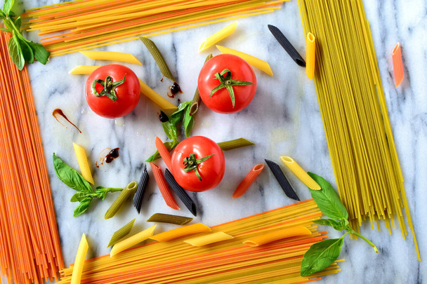 Cooking Italian pasta dish -- multicolored dry pasta, fresh tomatoes, basil on a marble board forming a rectangle frame - Photo, Image
