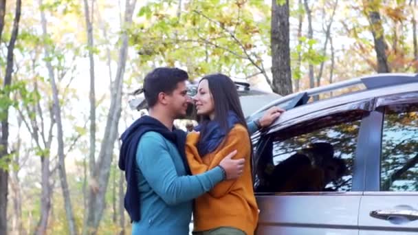 Αργή κίνηση πλάνο του ρομαντικού ζευγαριού, άντρας και γυναίκα στην αγάπη κοιτάζονται με χαμόγελο κοντά στο αυτοκίνητο στο δάσος του φθινοπώρου. Ξερά φύλλα πέφτουν πάνω τους. - Πλάνα, βίντεο