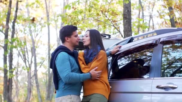 Αργή κίνηση πλάνο του ρομαντικού ζευγαριού, άντρας και γυναίκα στην αγάπη κοιτάζονται κοντά στο αυτοκίνητο στο δάσος του φθινοπώρου. Ξερά φύλλα πέφτουν πάνω τους. - Πλάνα, βίντεο