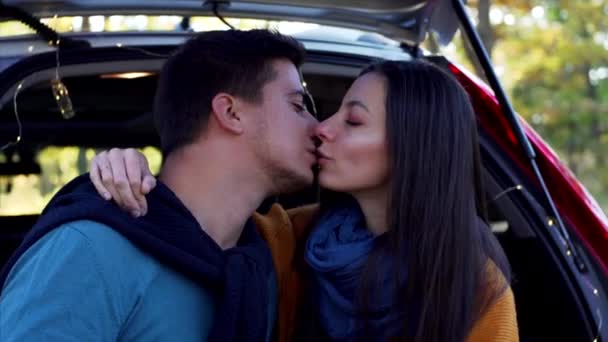 Νεαρό ερωτευμένο ζευγάρι φιλιέται στο πορτ-μπαγκάζ του αυτοκινήτου στο γραφικό δάσος του φθινοπώρου - Πλάνα, βίντεο