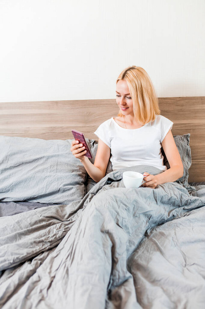 Beautiful young woman using phone in bed - Fotografie, Obrázek