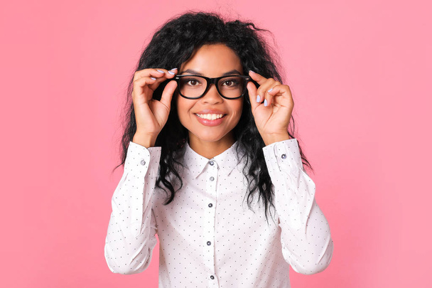 beautiful mixed race woman wearing eyeglasses and looking at camera on pink studio background  - Foto, immagini