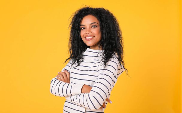 beautiful mixed race woman standing with crossed arms and looking at camera on yellow studio background  - Fotoğraf, Görsel