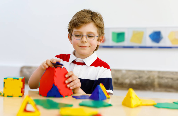 Счастливый мальчик в очках весело строит и создает геометрические фигуры, изучает математику и геометрию - Фото, изображение