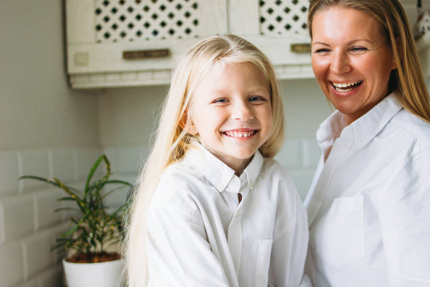 Счастливая блондинка с длинными волосами мама и дочь веселятся на кухне, ведут здоровый семейный образ жизни
 - Фото, изображение