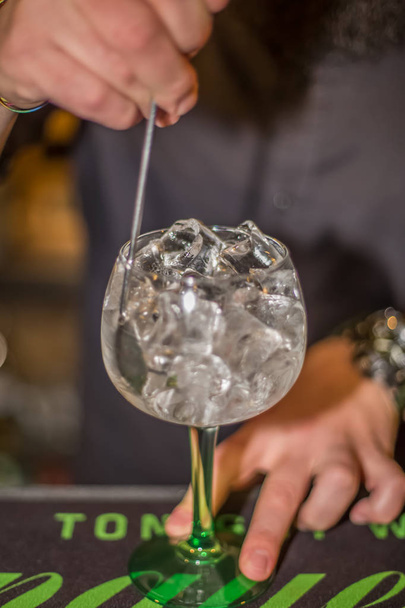 Näkymä baarimikko valmistelee lasi tonic gin pullossa paljon jäätä baarissa juomia
 - Valokuva, kuva