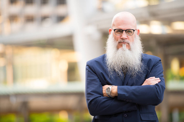 Mature bearded bald businessman with arms crossed in the city outdoors - Foto, Imagem