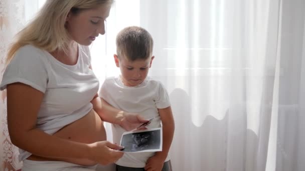 беременная женщина с сыном показывает сканирование будущего ребенка дома
 - Кадры, видео