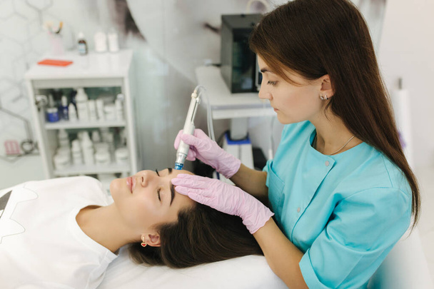 Professional female cosmetologist doing hydrafacial procedure for beautiful girl. Soft skin. Cosmetology clinic - Photo, Image
