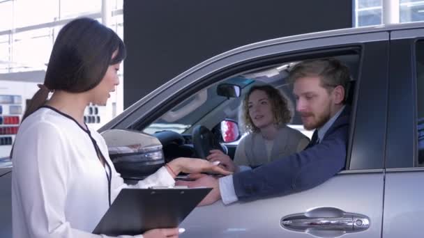 profesionální manažer asijské fena informuje kupující mladá rodina sedí v autosalonu při nákupu auta v autosalonu - Záběry, video