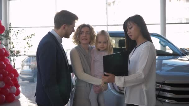 koupě vozidla, šťastný pár s malým dítětem informuje s automobilovým poradcem o koupi rodinného automobilu v prodejně - Záběry, video
