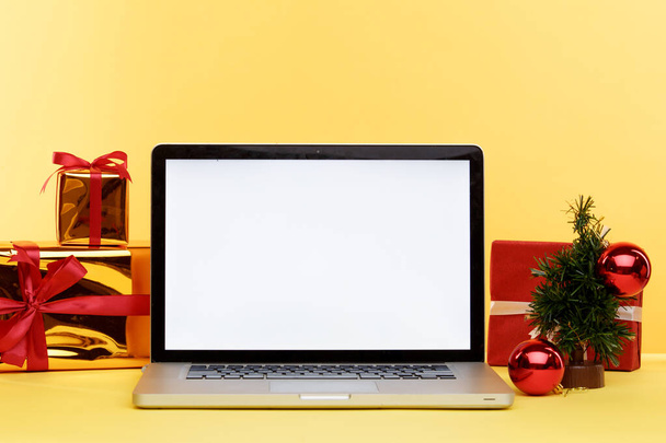 Online Χριστούγεννα έννοια ψώνια στην οθόνη του φορητού υπολογιστή. Λευκή οθόνη στον υπολογιστή και δώρα με χάρτινες σακούλες κοντά. - Φωτογραφία, εικόνα