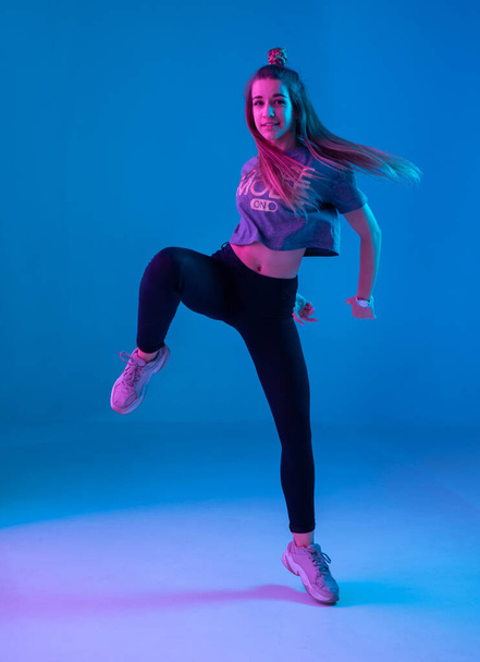 Νεαρό κομψό κορίτσι που χορεύει ζούμπα στο στούντιο σε έγχρωμο φόντο νέον. Σχεδιασμός αφίσας χορού. - Φωτογραφία, εικόνα