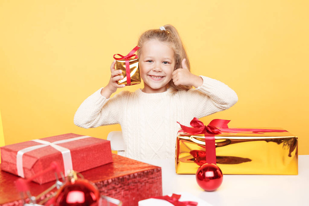 Glad girl with presents sitting isolated over the yellow studio. - Foto, Imagem