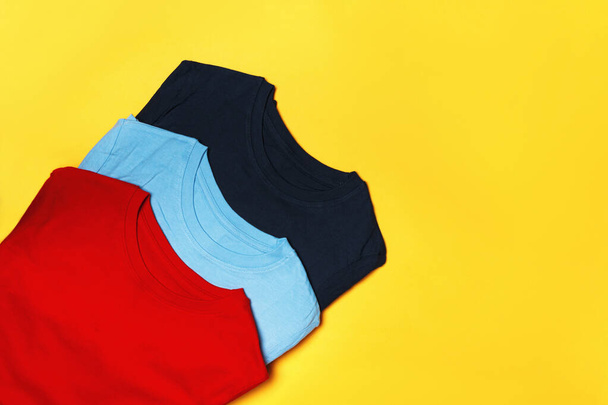 Top view of a composition with multi-colored t-shirts on a yellow background. Copy space - Foto, afbeelding