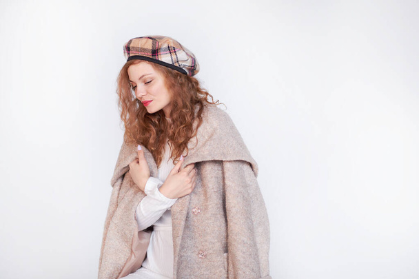 Beautiful girl dressed in french style on a white background. red hair woman is wrapped in a coat, winter clothes. Smiling lady wearing warm clothes, winter portrait - Foto, immagini