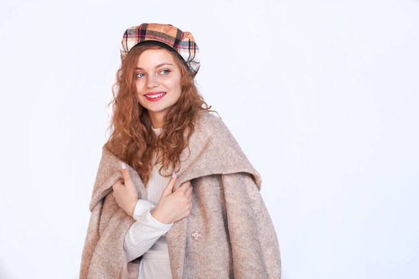 Beautiful girl dressed in french style on a white background. red hair woman is wrapped in a coat, winter clothes. Smiling lady wearing warm clothes, winter portrait - Photo, Image