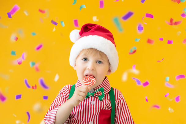 Happy child holding lollipop in hand against yellow background - Foto, afbeelding