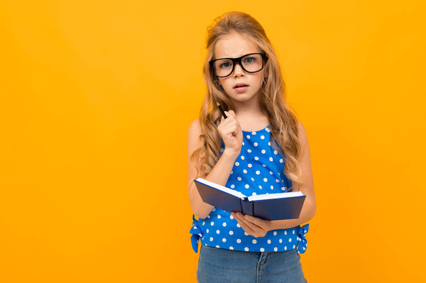маленькая умная девочка позирует в очках и блокноте на оранжевом фоне
   - Фото, изображение