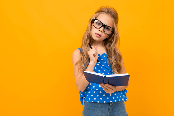 little smart girl posing with eyeglasses and notebook against orange background   - Photo, Image