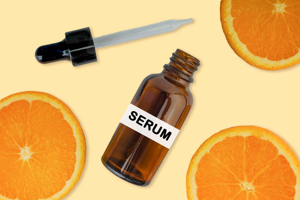 Vitamine C serum in cosmetische fles met druppelaar, gesneden sinaasappel op witte achtergrond. Gezondheidszorgconcept - Foto, afbeelding
