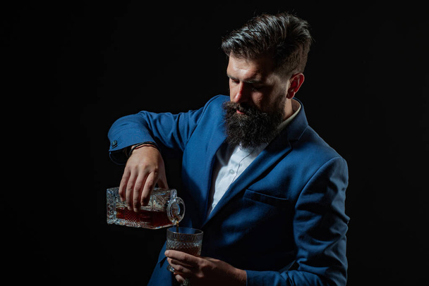 Hipster with beard and mustache in suit drinks alcohol after working day. Sommelier tastes expensive alcohol drink. - Foto, afbeelding