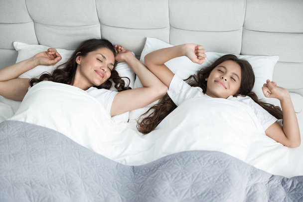 young beautiful mother and her cute teen daughter just woke up together in bed both stretchin - Photo, image
