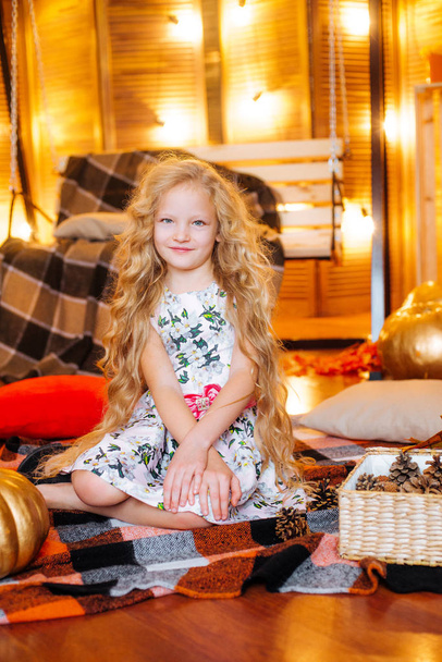 Cute girl of school age with blond long hair in  dress an autumn studio with yellow leaves, plaids, pumpkins and apples - Foto, Bild