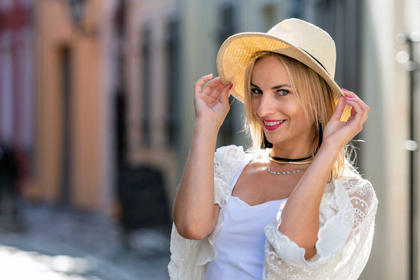Portrait of beautiful blond woman with sun hat dressed in  light clothes. Trendy girl posing in the street background. - Foto, immagini