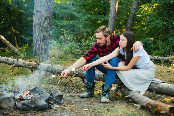 Summer lifestyle. Couple in love having hike picnic nature background. Funny couple eating roasted marshmallows while camping near the lake. Couple in love enjoying picnic in the forest. - Foto, Imagen