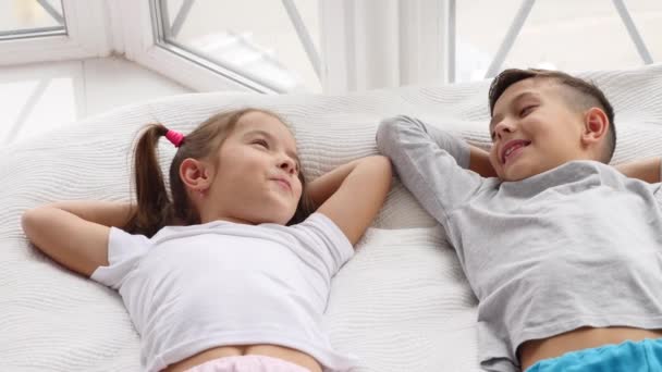 Top view on two beautiful siblings lying on a bed together, smiling and talking while having a rest. - Záběry, video