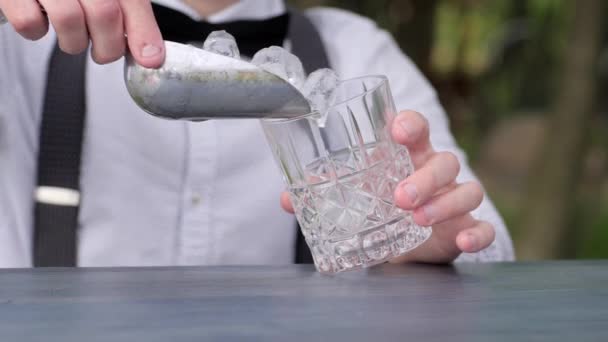 baarimikko laittaa jääpaloja lasiin baaritiskillä, mies baarimikko lisää jääpaloja lasiin alkoholia, Cocktail Party
, - Materiaali, video