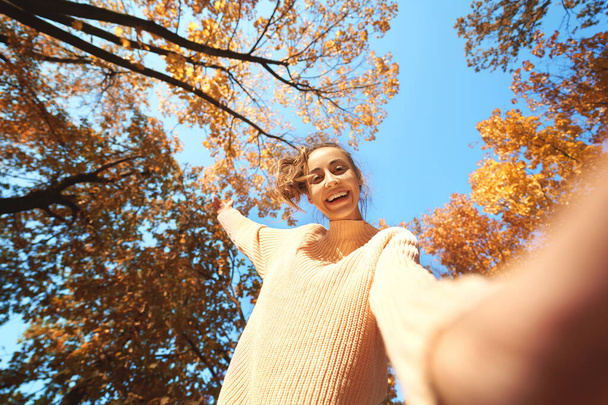 κάτω όψη του χαρούμενου κοριτσιού γέλιο κοιτάζοντας κάτω και παίζοντας αποξηραμένα κίτρινα φύλλα. - Φωτογραφία, εικόνα
