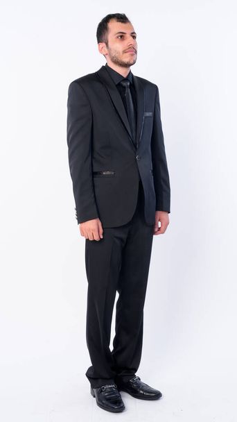 Full body shot of young bearded Persian businessman in suit thinking - Foto, afbeelding