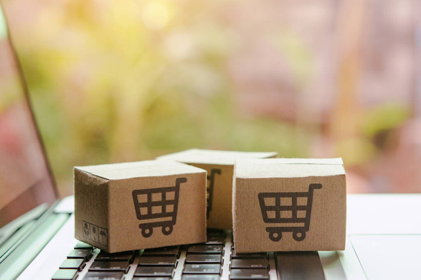 Online nakupování - Papírové krabice nebo balíček s logem nákupního košíku na klávesnici notebooku. Nákupní servis na webu a nabízí doručení domů - Fotografie, Obrázek