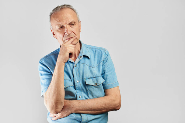 Pensive pensioner looks skeptically to the side, holds his chin and thinks on a white background isolated - Photo, image