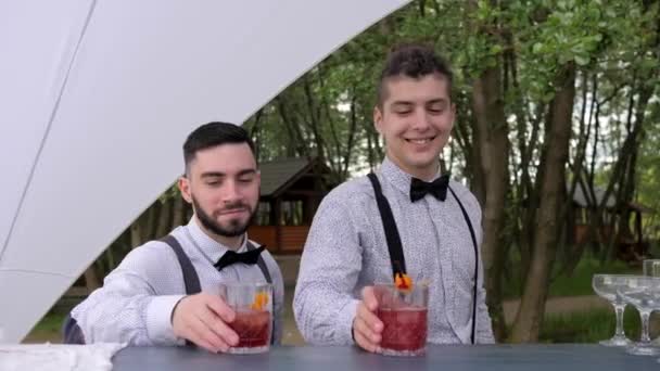 glimlachende barmannen achter de bar serveert cocktail, barman het maken van koele drank in glas, barman versieren cocktails - Video