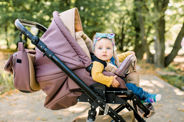 Cute little beautiful baby girl sitting in the pram or stroller and waiting for mom. Happy smiling child with blue eyes. - Fotografie, Obrázek