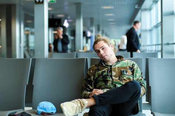 Καυκάσιος ο άνθρωπος που κάθεται στην αίθουσα αναμονής στο αεροδρόμιο και ακούτε μουσική. - Φωτογραφία, εικόνα