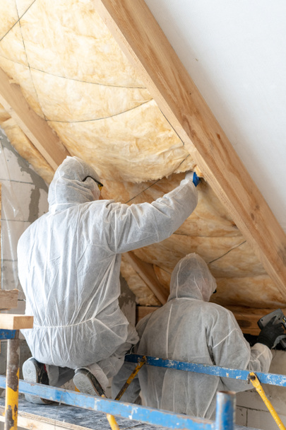 Δύο επαγγελματίες οικοδόμος άνθρωπος εγκατάσταση θερμομόνωση πετροβάμβακα κάτω από την οροφή - Φωτογραφία, εικόνα
