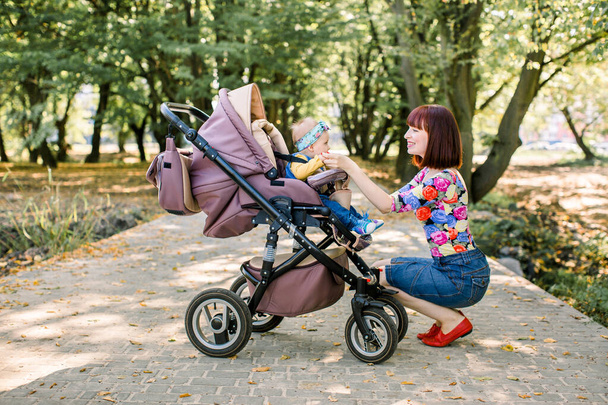 Jovem mãe olhando para seu filho em um carrinho de bebê
 - Foto, Imagem