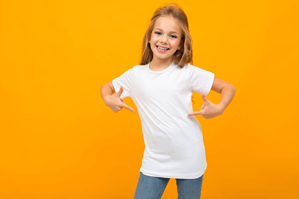 cute little girl in jeans and white t-shirt posing against orange background  - Foto, immagini