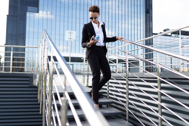 bela mulher de negócios posando ao ar livre contra edifício moderno com telefone e garrafa de água
 - Foto, Imagem