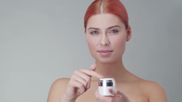 Studio portrait of young, beautiful and natural redhead woman applying skin care cream. Face lifting, cosmetics and make-up concept. - Кадры, видео